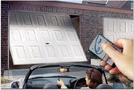 Person opens a garage door with a remote while sitting in a convertible car.