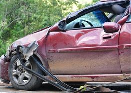 Red car with a crushed front and shattered windshield after an accident, shown on a clear day.