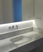 Baño moderno con lavabo de mármol blanco, grifo en la pared e iluminación LED suave.