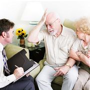 Elderly couple consulting with an advisor, man touching his forehead, woman looking concerned.