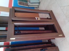 Finestra di legno appoggiata a parete, con telaio marrone e maniglia dorata, su pavimento piastrellato.