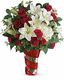 Bouquet of red roses, white lilies, and greenery in a red glass vase.