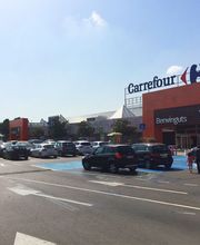 Entrada del supermercado Carrefour con varios coches aparcados en el parking.