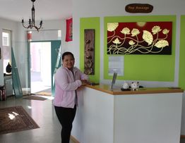 Frau an Empfangstheke eines Thai-Massage-Studios mit grüner Wand und Lotusbild.