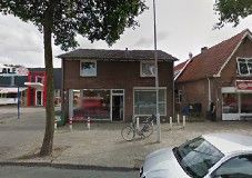 Een straatbeeld met een bakstenen gebouw, een fiets geparkeerd en enkele auto’s op de voorgrond.