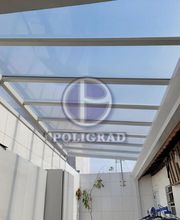 Cobertura translúcida em estrutura metálica sobre pátio com paredes brancas.