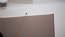 Person adjusting a wall-mounted object with a long rod near a ceiling fan.
