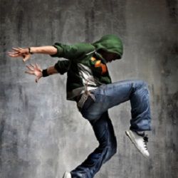 Person in green hoodie and jeans jumping dynamically against a textured gray background.