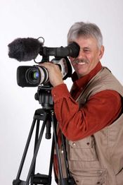 Ein lächelnder Mann filmt mit einer großen Videokamera auf einem Stativ.