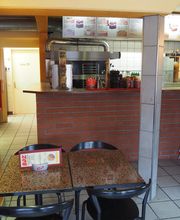 Kleines Restaurant mit Theke, zwei Tischen, Bestelltresen und Stühlen in schlichter Einrichtung.