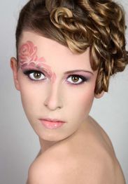 Frau mit kunstvollem Make-up und Lockenfrisur, rosa Blütendesign über dem rechten Auge.