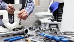 Installateur arbeitet an Rohren, mit Werkzeugen auf dem Boden. Badezimmer im Hintergrund.