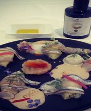 Piatto gourmet con pesce, fiori ed erbe su piatto nero. Bottiglia di olio a lato.