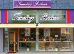 Geschäftsfassade von "Trauring Partner" mit großen Fenstern und offener Eingangstür.