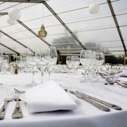 Elegant table setting with glasses and cutlery under a clear tent roof.