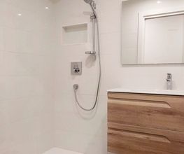 Baño moderno con ducha, espejo y lavabo con cajones de madera.