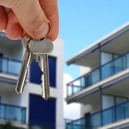 Hand holding keys with modern apartments in the background.