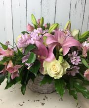 Arreglo floral con lirios rosados, rosas blancas y margaritas. Fondo de madera blanca.