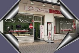 Nagelstudio "City Nails" mit Schaufenstern, Logo und Preisen. Straße spiegelt sich in Fenstern.
