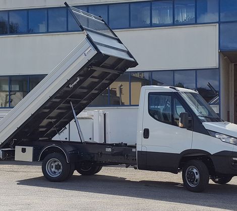 Camion bianco con cassone ribaltabile sollevato in un cortile di fronte a un edificio.