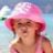Ein Kind mit rosa Hut am Strand, lächelnd und das Meer im Hintergrund.