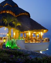 Casa con techo de paja iluminada junto al mar al atardecer.