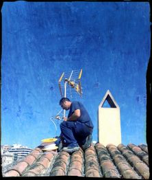 Hombre trabajando en el techo, instalando una antena bajo un cielo azul claro.