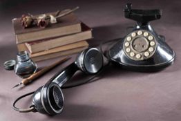 Altes schwarzes Wählscheibentelefon, Bücher und Schreibfeder auf einem Tisch.