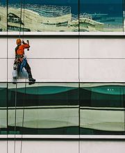 Operai su una facciata di vetro di un edificio, indossano caschi e attrezzatura di sicurezza.