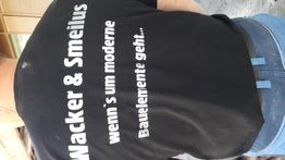 Schwarzes T-Shirt mit weißem Text: "Wacker & Smelius, wenn's um moderne Bauelemente geht...".