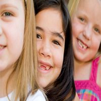 Three smiling children with missing teeth, close to the camera.