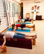 Personas haciendo yoga en un estudio con bloques de madera y equipos en la pared.
