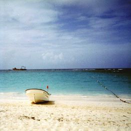 Strand mit Boot im Vordergrund, ruhiges Meer und bewölkter Himmel im Hintergrund.