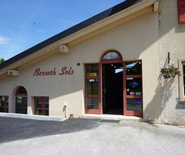Gebäude mit der Aufschrift "Bersetth Sols", roter Tür und Blumen an der Wand, bei Sonnenschein.
