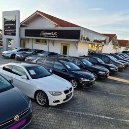 Gebrauchtwagen auf einem Parkplatz vor einem Autohaus mit Werbetafel.