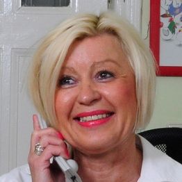 Eine lächelnde Frau mit blondem Haar telefoniert.