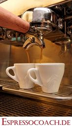 Espressomaschine füllt zwei Tassen mit frischem Espresso, darunter die Webseite espressocoach.de.