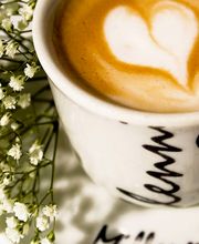 Tazza di cappuccino con un cuore nella schiuma accanto a fiori bianchi.