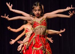 Young dancers in red costumes perform, arms extended, creating a visual effect on stage.
