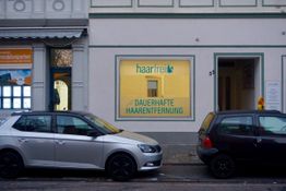 Zwei Autos vor einem Geschäft für dauerhafte Haarentfernung in einer städtischen Straße geparkt.