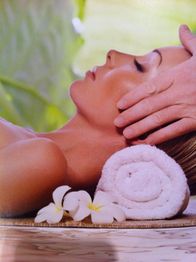 Frau entspannt bei Kopfmassage, Kopf auf Handtuch, Blumen im Vordergrund.