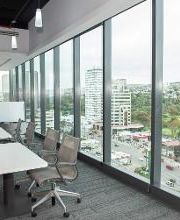 Oficina moderna con mesas, sillas y ventanales que muestran la vista de una ciudad.