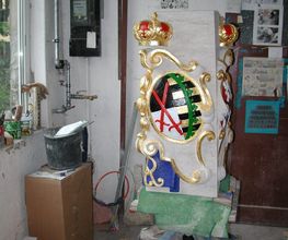 Wappenverzierte Steinsäule in Werkstatt, umgeben von Werkzeugen und Bauutensilien.