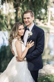 Couple in wedding attire embracing, with a blurred natural background.