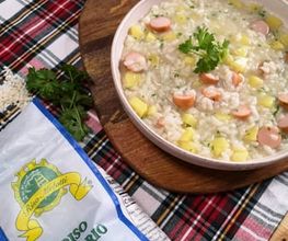 Teller mit Risotto, Würstchen und Gemüse auf Holzbrett. Daneben Riso Arborio-Reispackung.