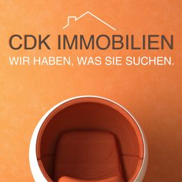 Orange Stuhl vor orangener Wand mit Schriftzug „CDK IMMOBILIEN: Wir haben, was Sie suchen.“