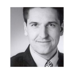 Porträt eines lächelnden Mannes mit Anzug und Krawatte in Schwarzweiß.