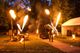 Feuershow im Freien mit Jongleur, Flammen und Zelt bei Nacht, Bäume im Hintergrund.
