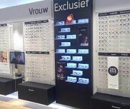 Wand met brillen op displays, onderverdeeld in "Vrouw" en "Exclusief". Diverse stijlen en prijzen.