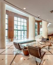 Saguão moderno com móveis elegantes, janelas grandes e escada ao fundo.